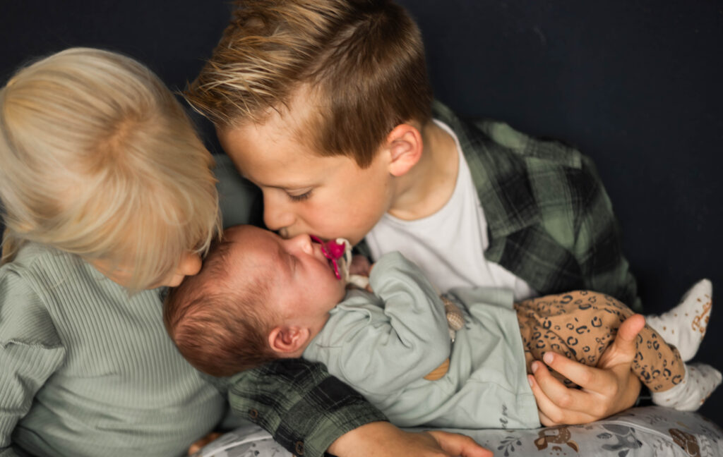 Grote broer en zus geven een kusje op het hoofdje van de newborn baby