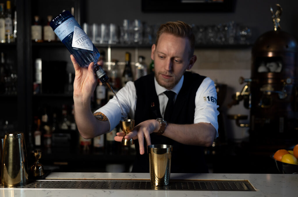 De mixologist schenkt de drank in de maatbeker